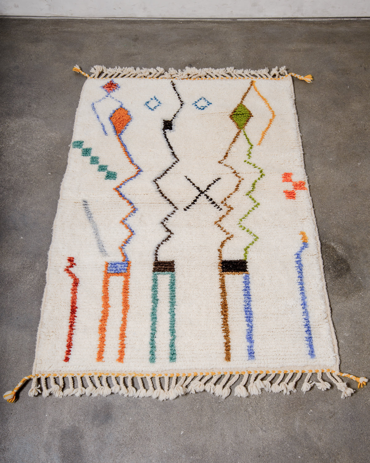 Berberlin special edition Beni Ourain rug made of cream wool with abstract design details featuring orange, brown, blue and khaki laying on concrete floor.